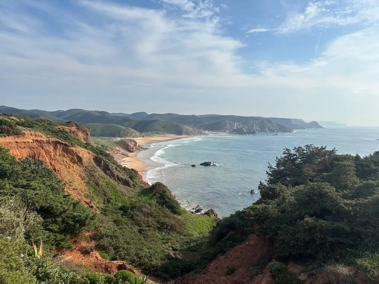Panoramic view of the Algarve coastline with red cliffs, green vegetation and a sweeping sandy bay