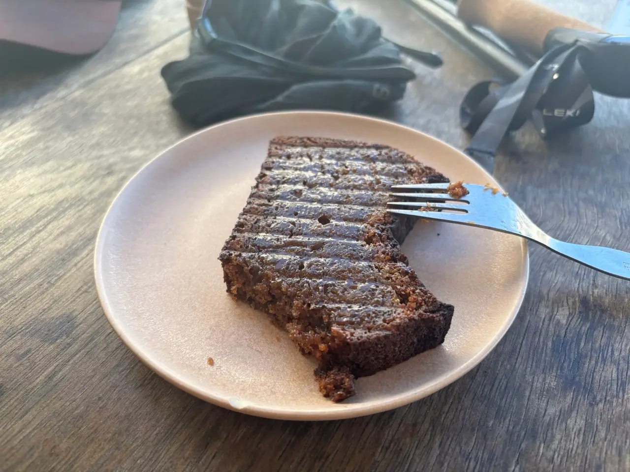 Thick slice of grilled banana bread on a plate with a fork, trekking pole visible on the wooden table