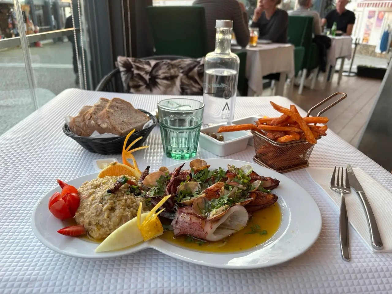Grilled squid and clams with sides of bread, olives and sweet potato fries on a restaurant table