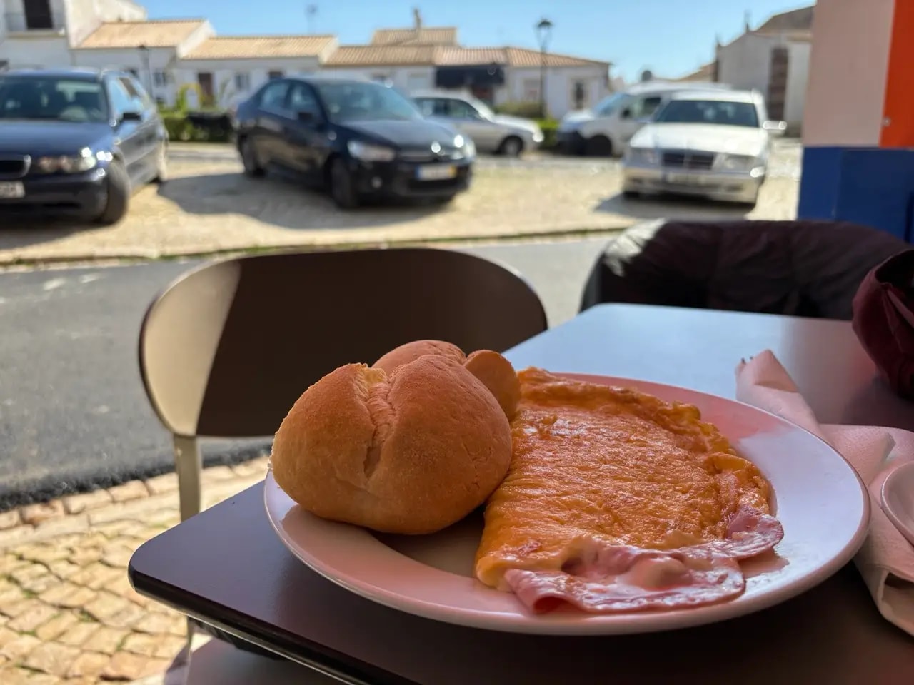 Ham omelette and bread roll on a plate at an outdoor café table