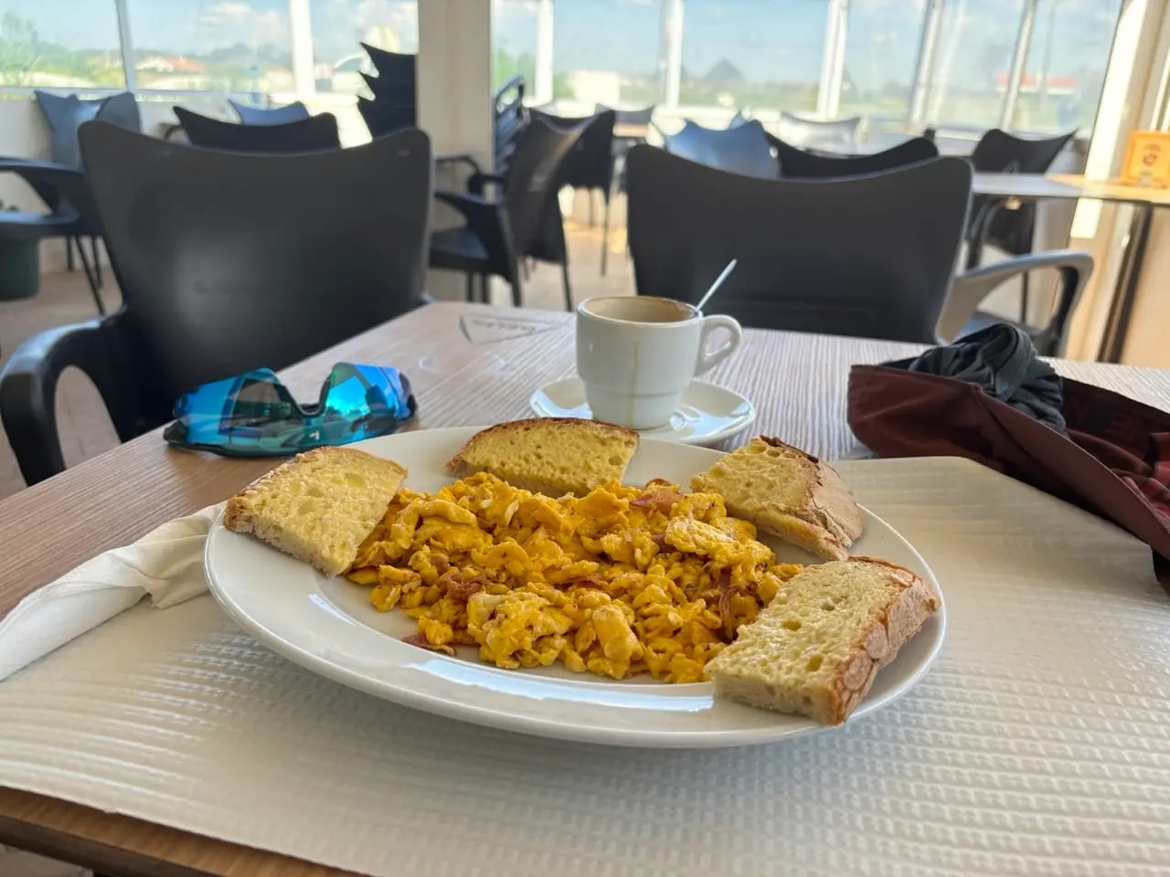 Scrambled eggs with meat and thick slices of bread on a plate with coffee on a clubhouse-style terrace