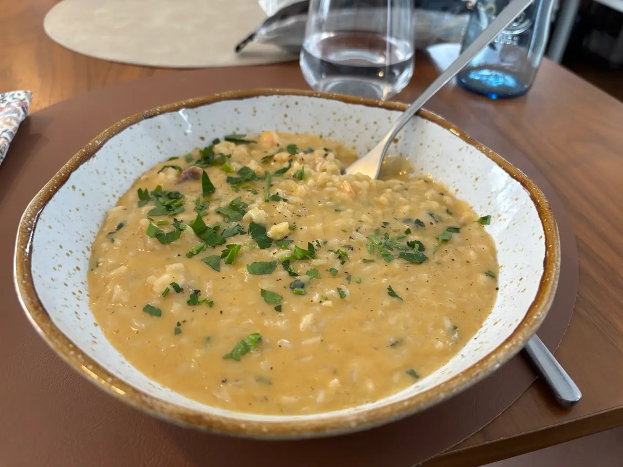 Creamy seafood rice in a rustic bowl with parsley and a spoon