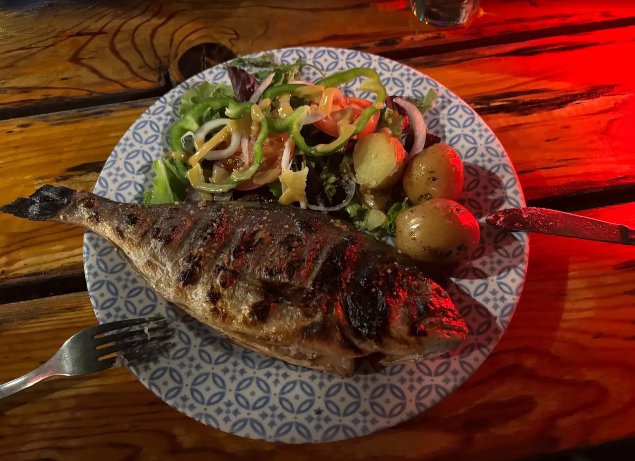 Whole grilled fish with salad and small potatoes on a patterned plate on a wooden table