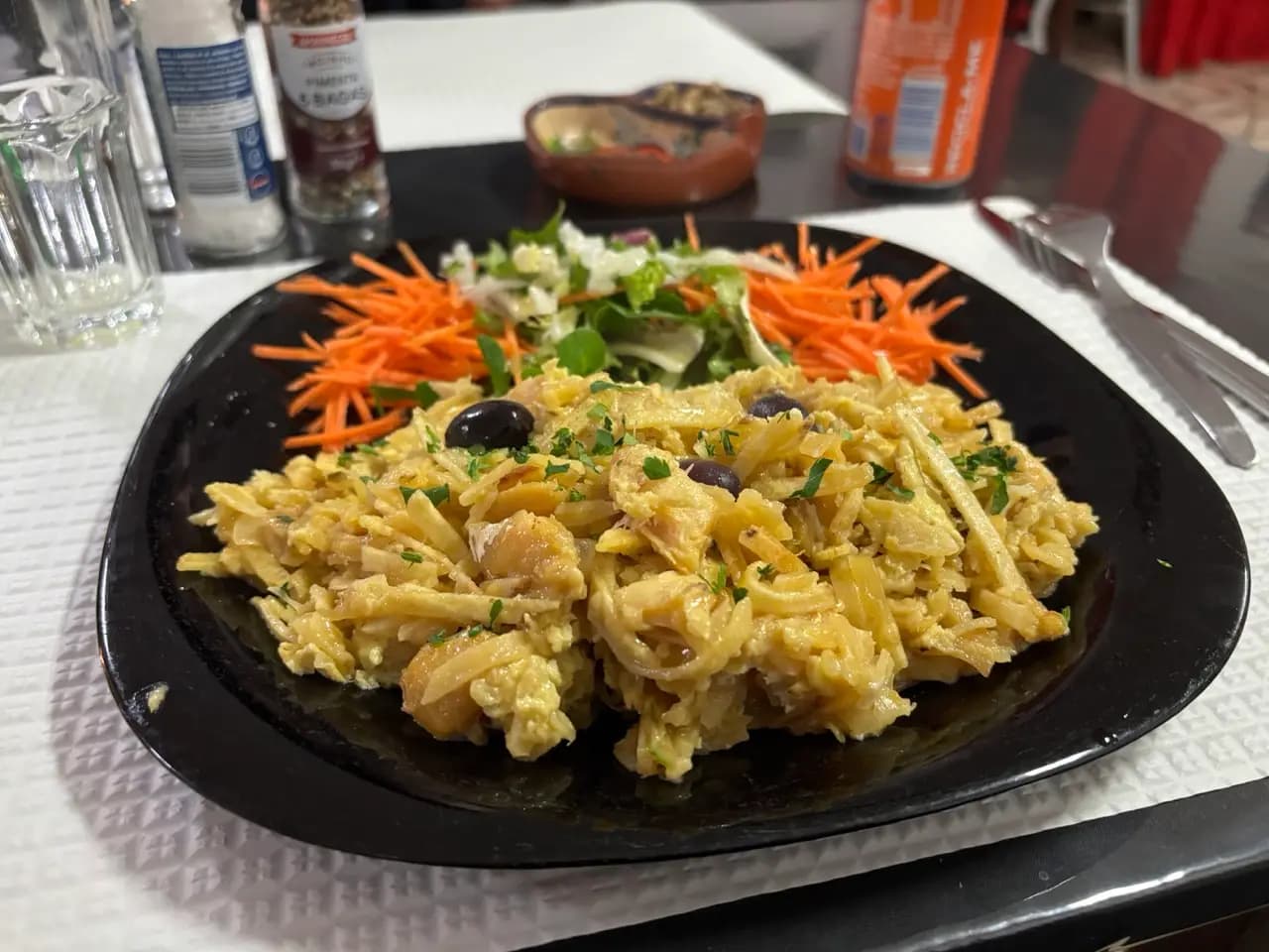 Bacalhau à Brás with shredded cod, egg and straw potatoes, olives and a side salad on a black plate Bacalhau à Brás with shredded cod, egg and straw potatoes, olives and a side salad on a black plate