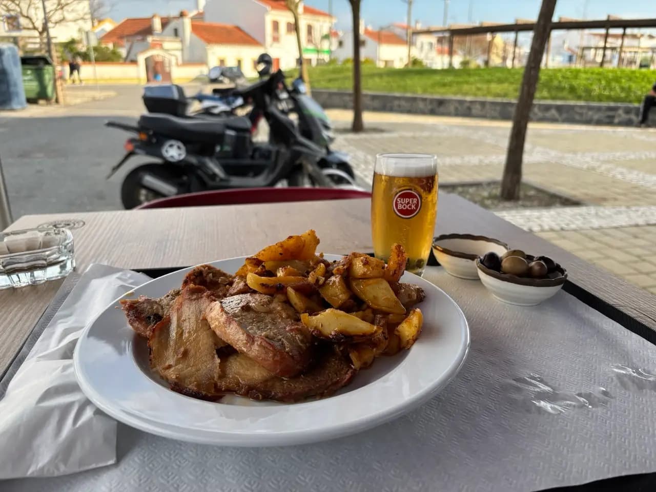Prato do dia with sliced roast meat, potatoes, olives and a glass of Super Bock on a terrace table Prato do dia with sliced roast meat, potatoes, olives and a glass of Super Bock on a terrace table