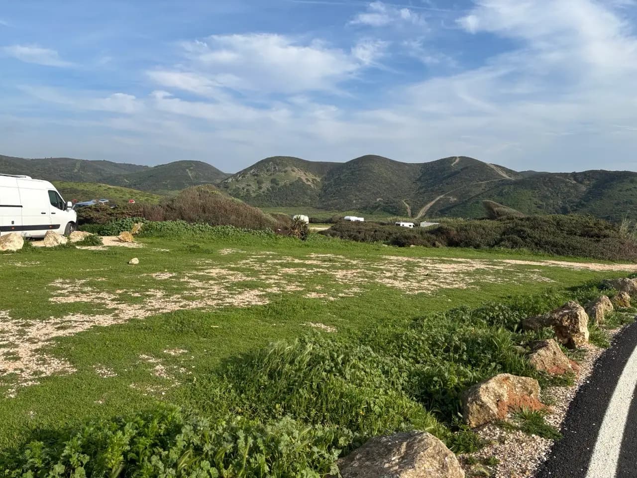 Camper vans on a grassy pull-off beside a road, rolling green hills and bright sky in the background Camper vans on a grassy pull-off beside a road, rolling green hills and bright sky in the background